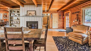 Interior rústico de una cabaña con una mesa de madera, sillas, chimenea y un sillón de cuero.