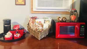 A kitchen area with a red microwave, a basket of snacks, a coffee maker, and an air conditioner.