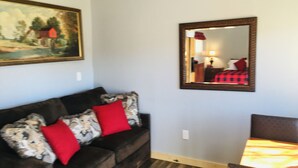 A living room with a dark brown sofa, red cushions, a framed painting, a mirror, and a patterned rug.