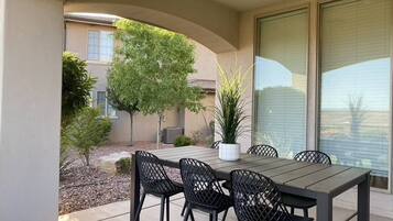 An outdoor patio with a table and chairs, surrounded by a garden and a building.
