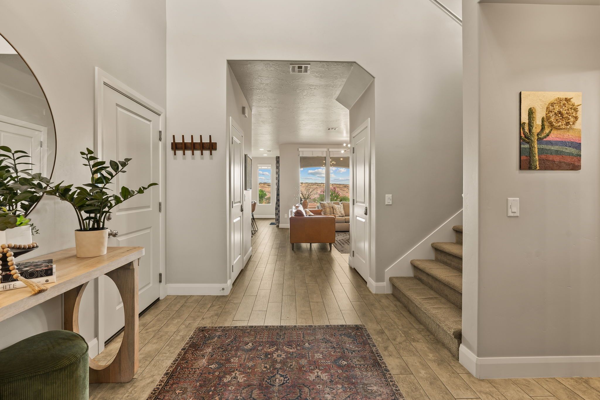 A hallway with a wooden floor, a bench, a table with a plant, and a door.