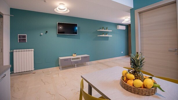 Un moderno salón con paredes color turquesa, una mesa blanca y una cesta de fruta.