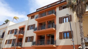 Un edificio de varios pisos con balcones, una palmera y cielo despejado.