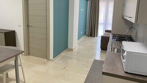 A modern kitchen with a stove, sink, and cabinets. There is a dining area with a table and chairs. The room has a door and a window with curtains. - Casa Marinara C: A modern and graceful apartment situated at a short distance from the beach, with Free WI-FI. (Balestrate)