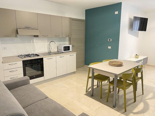 Une cuisine compacte équipée d’une cuisinière à gaz, d’un four à micro-ondes et d’un évier. Un coin repas avec une table et des chaises est également disponible.