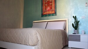Ein Schlafzimmer mit einem Bett, einem Nachttisch, einem Kaktus und einer Wanddekoration.