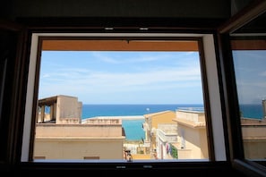 Une vue à travers la fenêtre d’un bâtiment situé sur la côte, avec un ciel dégagé et la mer en arrière-plan.