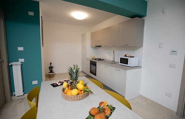 Une cuisine moderne avec des meubles blancs, un four à micro-ondes et une table à manger agrémentée de fruits et de pain.
