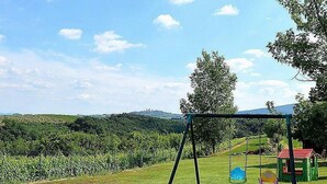A playground with swings and a slide, surrounded by lush greenery and a clear sky.