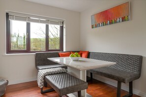 Un comedor moderno con una mesa blanca, un banco acolchado gris y un cuenco de fruta.