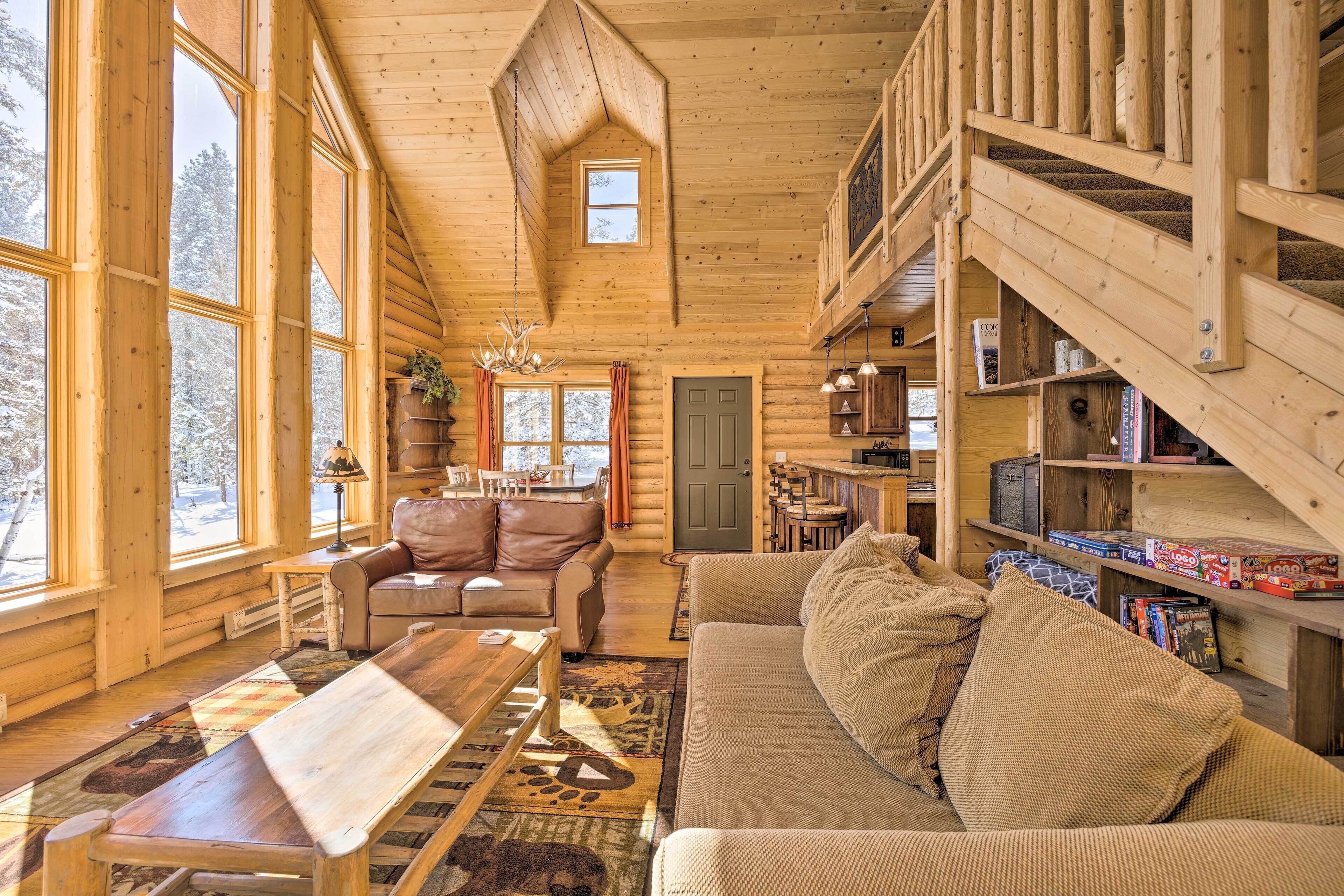 A log cabin interior with a wooden staircase, a sofa, a dining table, and a bookshelf.