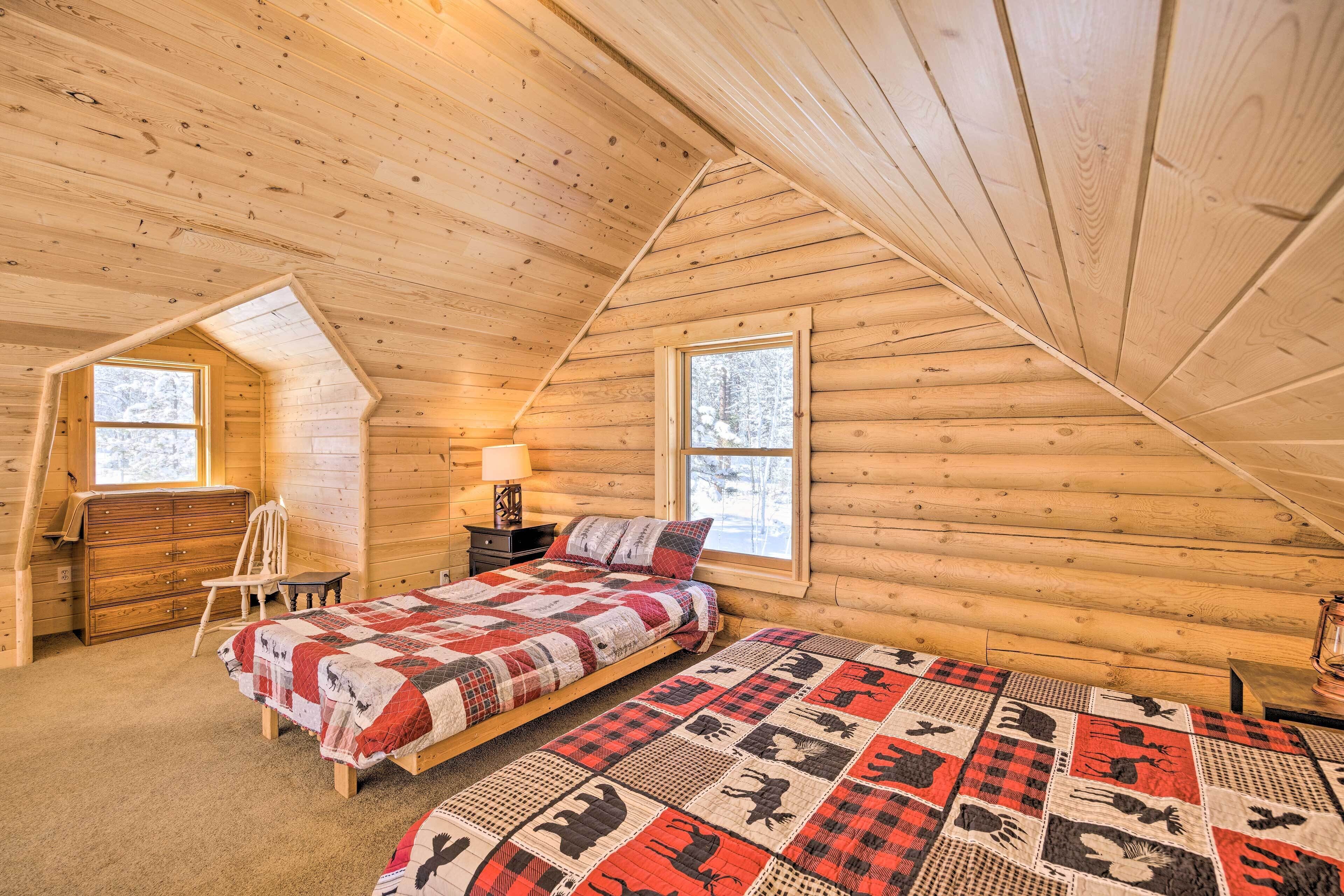 Une chambre confortable dans un chalet en rondins, avec un lit en mezzanine, une commode en bois et une fenêtre donnant sur la forêt enneigée.