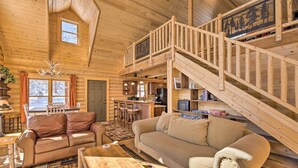 Ein Blockhaus-Innenraum mit einer Holztreppe, einem Essbereich, einer Küche und einem Wohnzimmer mit Sofa und Couchtisch.