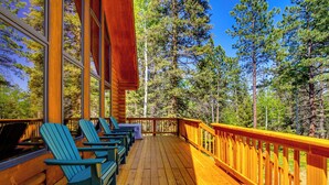 Eine Holzterrasse mit Adirondack-Stühlen, einem Hollerdgeschoss und Blick auf einen Wald.