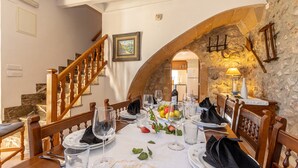 Un comedor con un arco de piedra, sillas de madera, mantel blanco y una escalera.