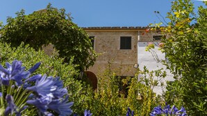 Un edificio de piedra con techo de tejas, rodeado de abundante vegetación y plantas florecientes.