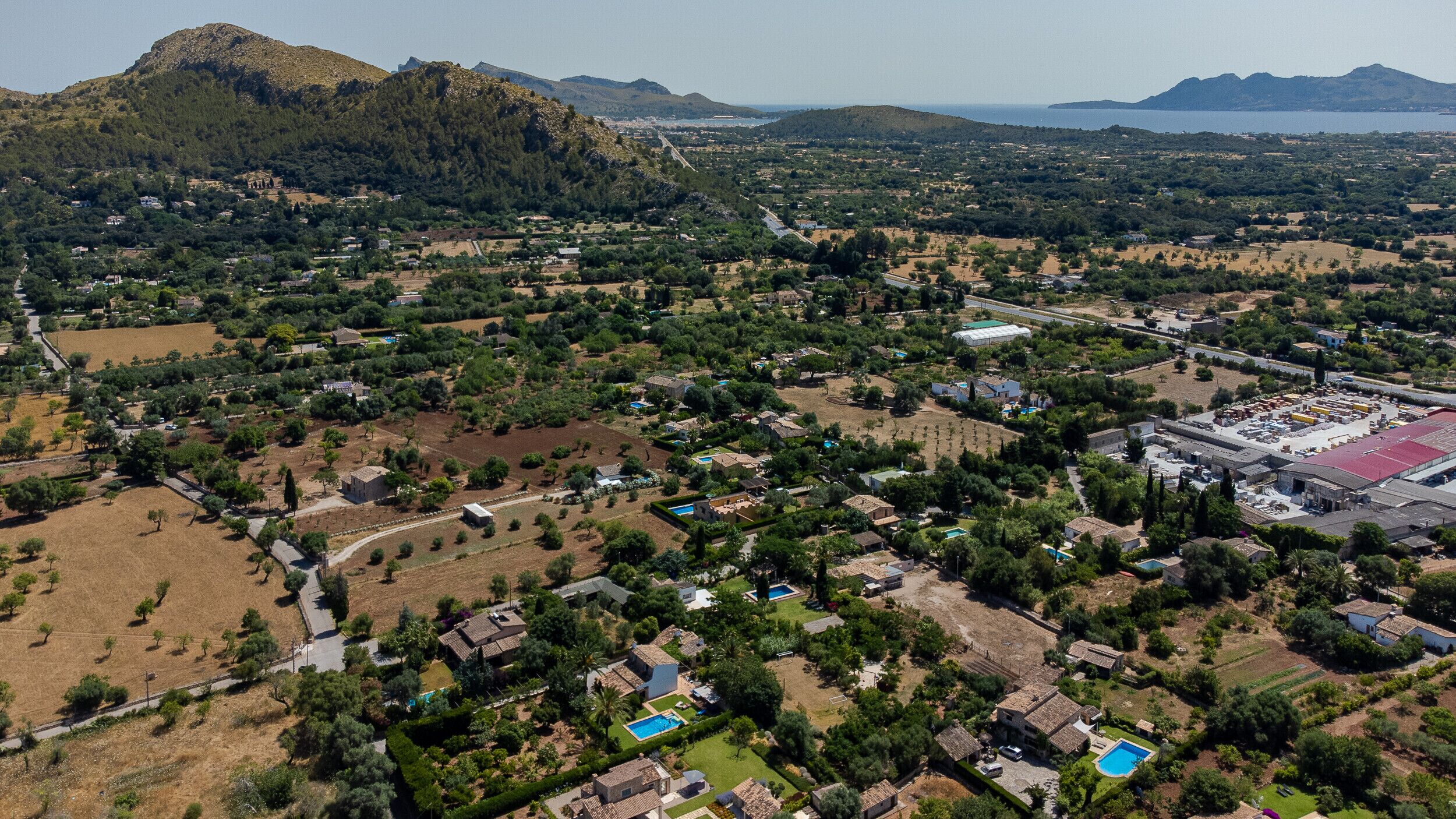 An aerial view of a coastal town with residential areas, green spaces, and a large industrial complex.