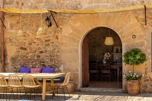 An outdoor seating area with a stone wall, wooden table, wicker chairs, and a potted plant. - Villa Lloquet in Pollensa by Home Villas 360 (Pollensa)