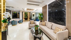 A modern living room with a sofa, coffee table, and patterned chairs. There is a large marble wall and a plant in the center. - Aprilis Deluxe Hotel (Istanbul)