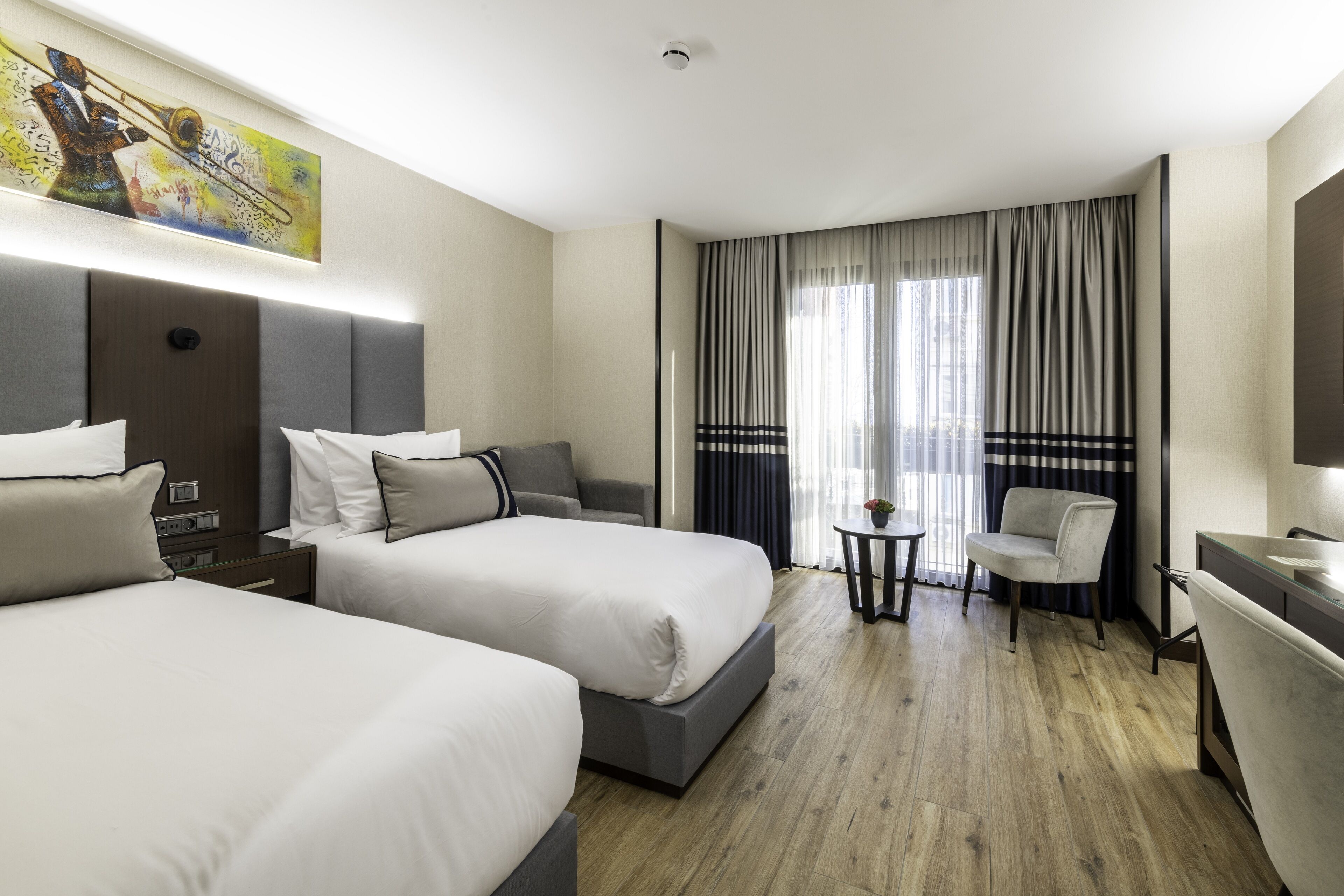 Habitación de hotel con dos camas, un escritorio, una silla y un ventanal con cortinas.