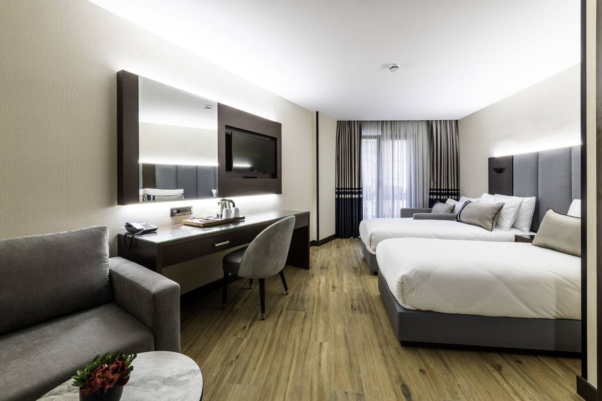 Una habitación de hotel con escritorio, dos camas, sofá y televisor.