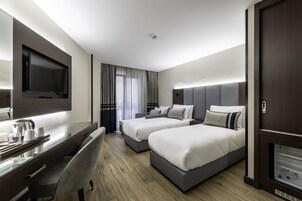 Una habitación de hotel con escritorio, dos camas, televisor y minibar.