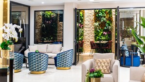 A modern living room with a sofa, two patterned ottomans, a coffee table, and a view of a garden through a glass door. - Aprilis Deluxe Hotel (Istanbul)