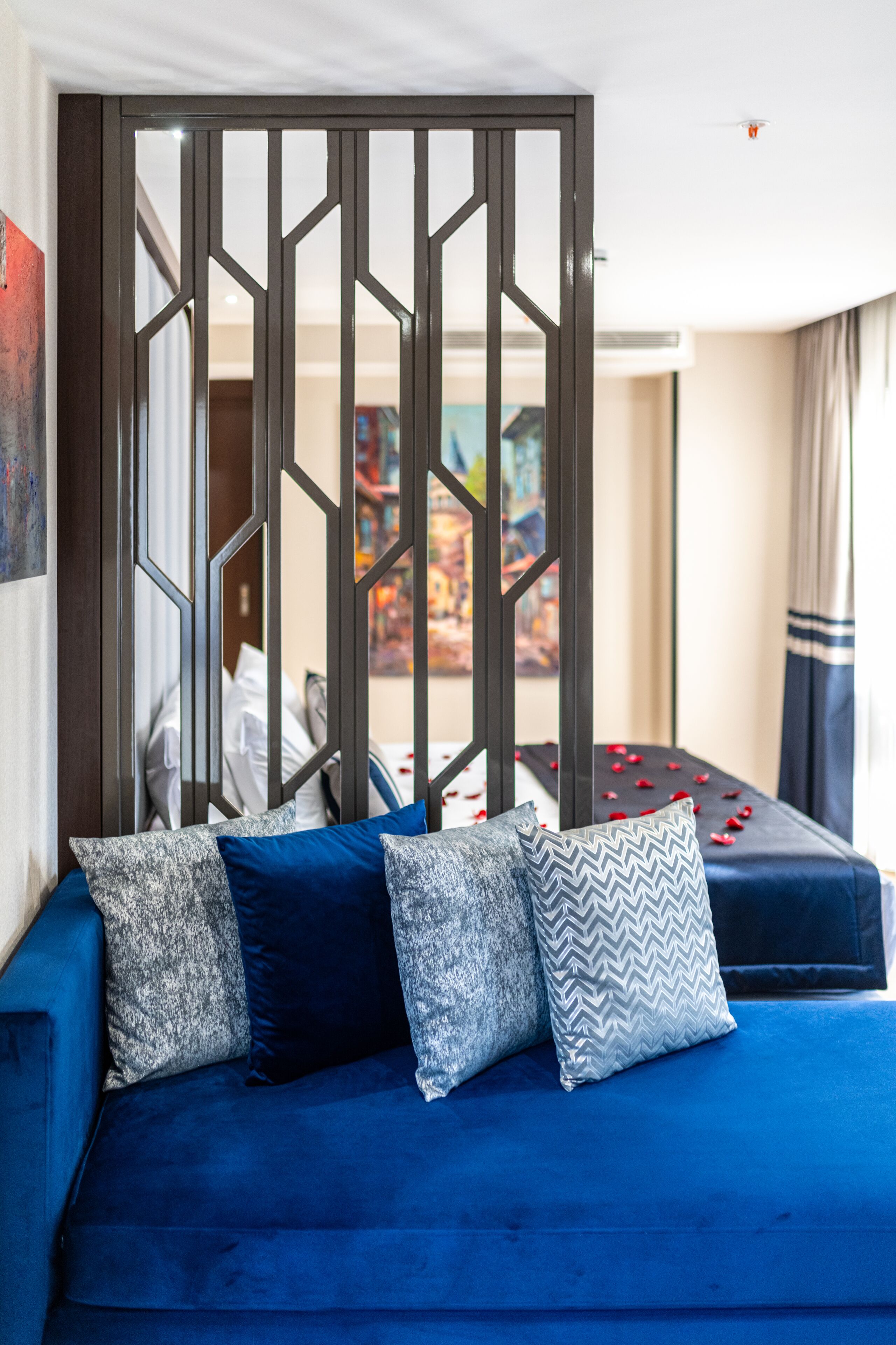 A blue sofa with patterned pillows, a decorative screen, and a painting in the background.