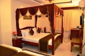 A four-poster canopy bed with a wooden frame, a bedside table, a chair, and a small table with a kettle.