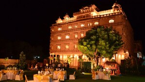 A grand building with multiple floors, ornate balconies, and a large tree in the foreground. - The Heritage Palace (Jaipur)