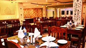 A restaurant with multiple dining tables set with white tablecloths, chairs, and various table settings including plates, glasses, and napkins. - The Heritage Palace (Jaipur)