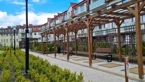 Ein überdachter Außenbereich mit Bänken und einer Straßenlaterne, umgeben von einem Garten und Wohnhäusern.