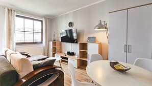 Ein modernes Wohnzimmer mit einer Couch, einem Fernseher, einem Esstisch und einer Lampe.