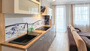 Eine moderne Küche mit integriertem Mikrowellenherd, einer Kaffeemaschine und einem Spülbecken. Es gibt einen Essbereich mit einer Bank und einem Fenster mit Vorhängen.