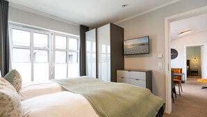 A modern hotel room with a large bed, a desk, and a view of the city through large windows. - Quartier Frohsinn, app. 11 (Heringsdorf)