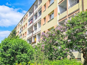 Un edificio residencial de varios pisos con balcones, cielo despejado y vegetación circundante.