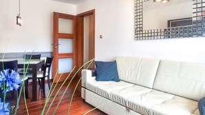 A living room with a sofa, a dining table with chairs, a wooden door, and a wall-mounted light fixture. - Matejki - Ma05 (Swinoujscie)