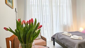 Een hotelkamer met een bed, een stoel, een tafel met een bloevas en een raam met dunne gordijnen.