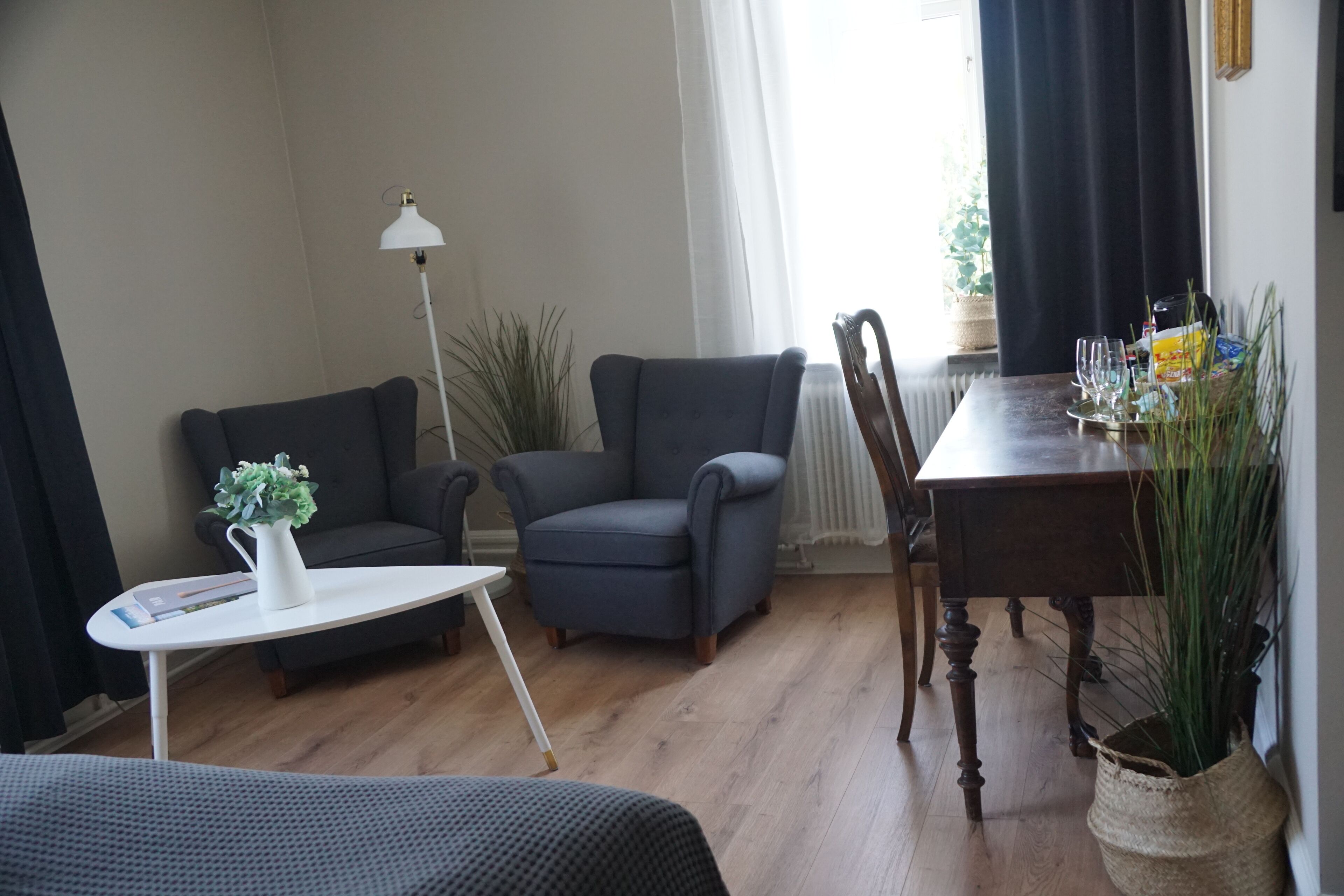 A cozy living room with a sofa, armchair, small table, and a dining table with chairs.