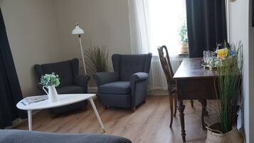 A cozy living room with a sofa, armchair, small table, and a dining table with chairs.