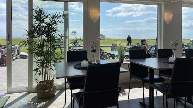 Un ristorante con ampie vetrate che si affacciano sul mare e su un campo da golf. Tavoli e sedie disposti per la ristorazione.