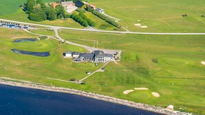 Vista aerea di un campo da golf con un club house, un’area parcheggio e uno specchio d'acqua.