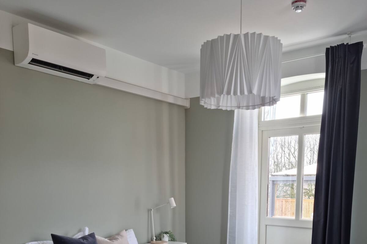 Quarto moderno com cama, mesa de cabeceira, abajur e janela com cortinas.