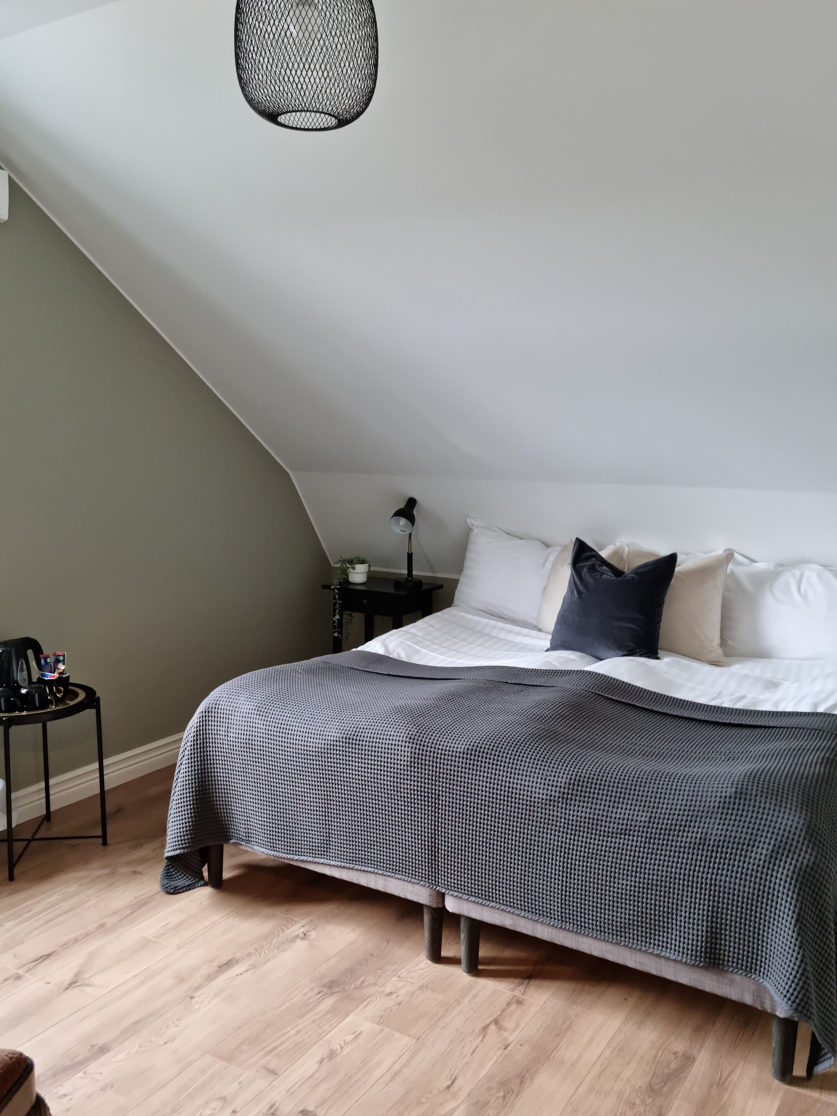 A bedroom with a bed, a nightstand, a lamp, and a coffee maker on a table.