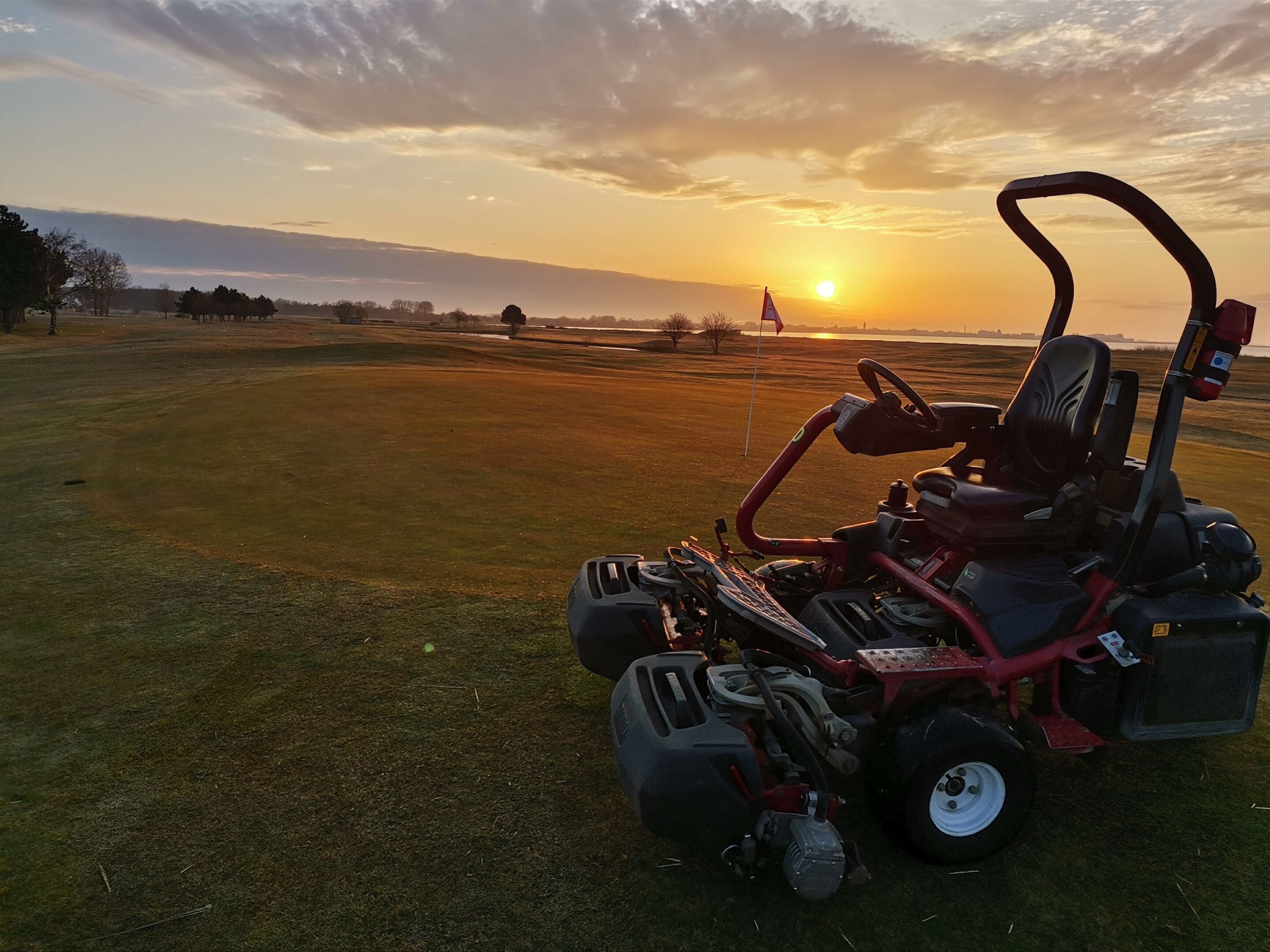 A lawnmower on a grassy field with a sunset in the background.