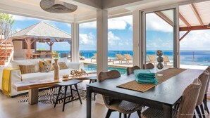 Una habitación amplia con una gran mesa de comedor, asientos cómodos, vista al océano y zona de piscina.