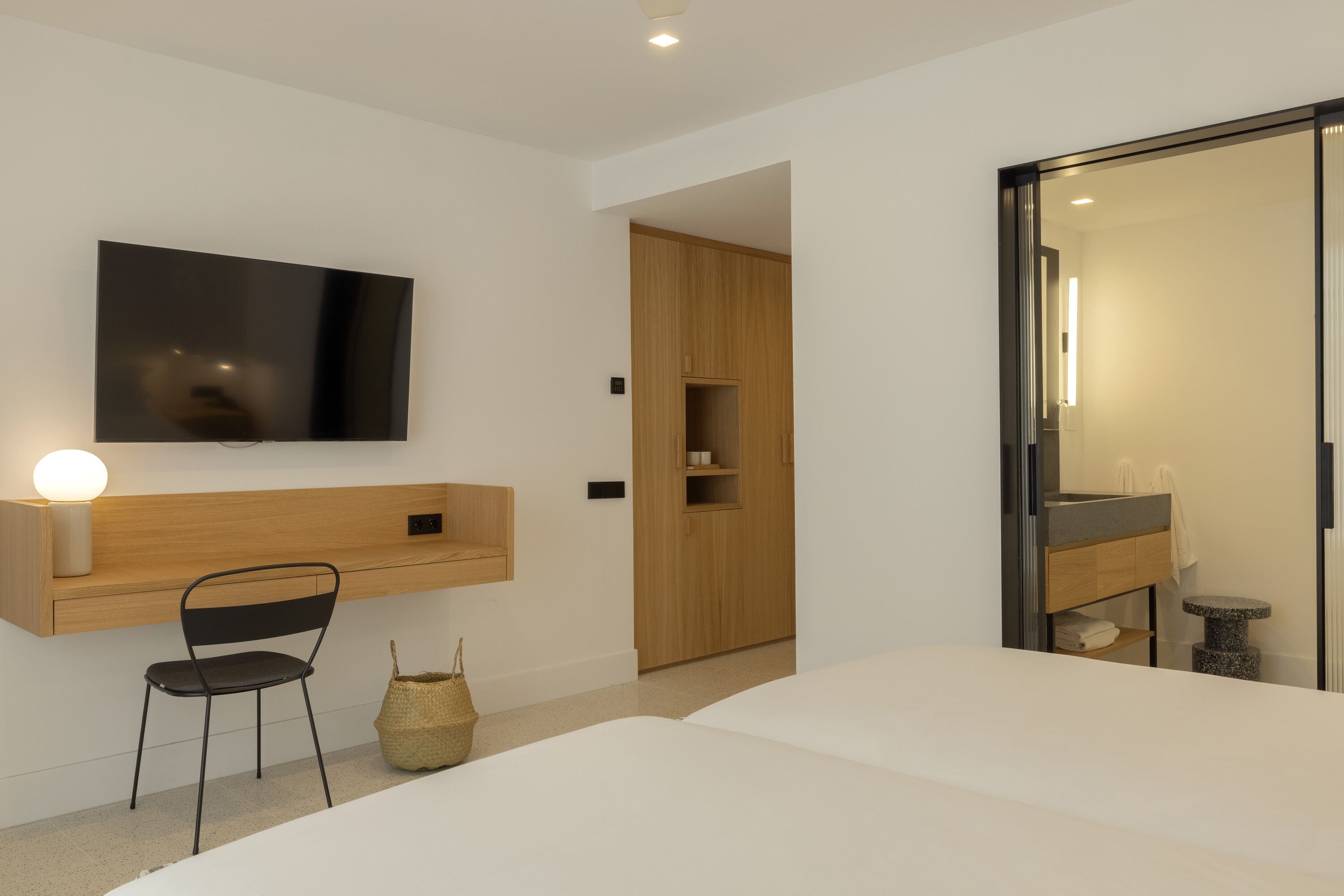 Un dormitorio moderno con una cama grande, un televisor montado en la pared, un escritorio de madera y un armario.