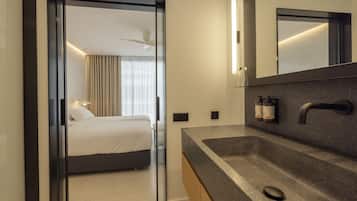 Une chambre d’hôtel moderne, équipée d’un lit, d’un grand miroir, d’un lavabo en granit et d’une porte donnant sur une autre pièce.