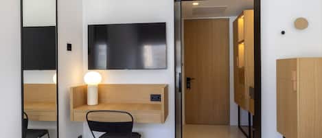 A hotel room with a bed, a desk with a chair, a TV, and a wardrobe.