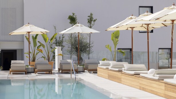 Ein Poolbereich mit Liegestühlen und Sonnenschirmen, ein klares Schwimmbecken und ein modernes Gebäude im Hintergrund.